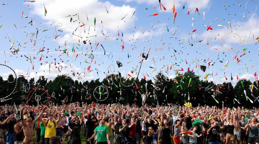 Photograph of a sea of people juggling, with very little of a field visible between legs and a blue sky filled with all kinds of objects